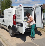 Une livreuse prend des plateaux-repas à l’arrière d’un véhicule de livraison blanc.