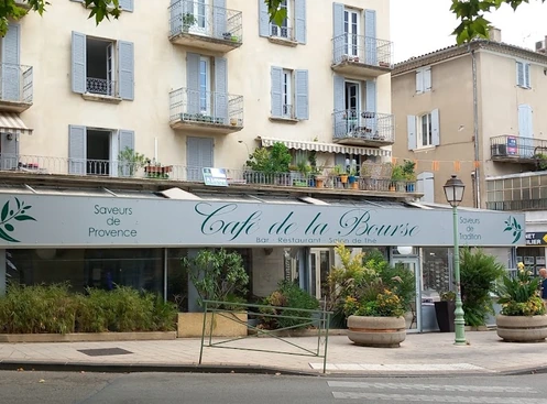 Façade du Café de la Bourse à Nyons, avec son enseigne et une terrasse entourée de plantes.