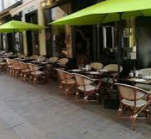 Tables et fauteuils de la terrasse de Lou Tex à Nyons sous des parasols verts