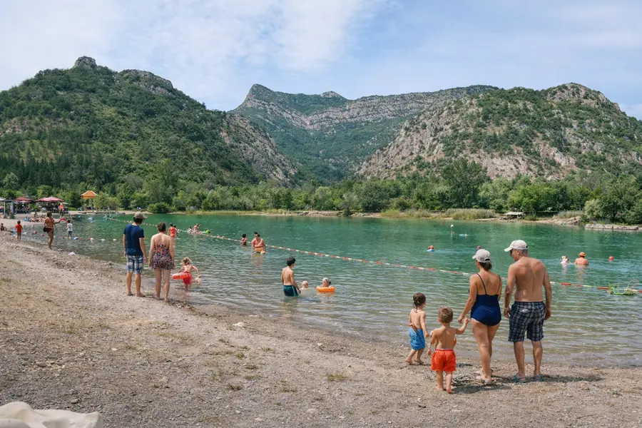 Familles sur la plage de galets et dans l’eau du lac du Pas des Ondes.