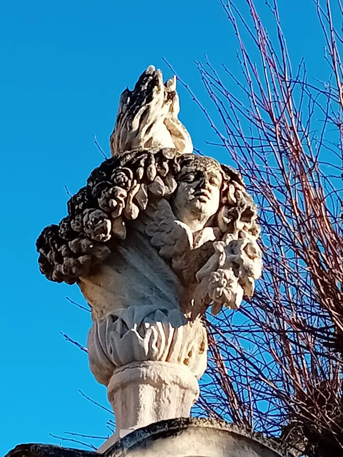 Sculpture de pierre sur la Tour Randonne à Nyons, avec des branches en arrière-plan.