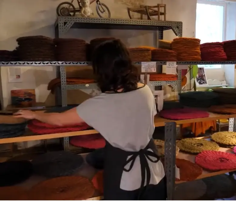 Artisane devant des scourtins colorés sur une table de l’atelier de Nyons.