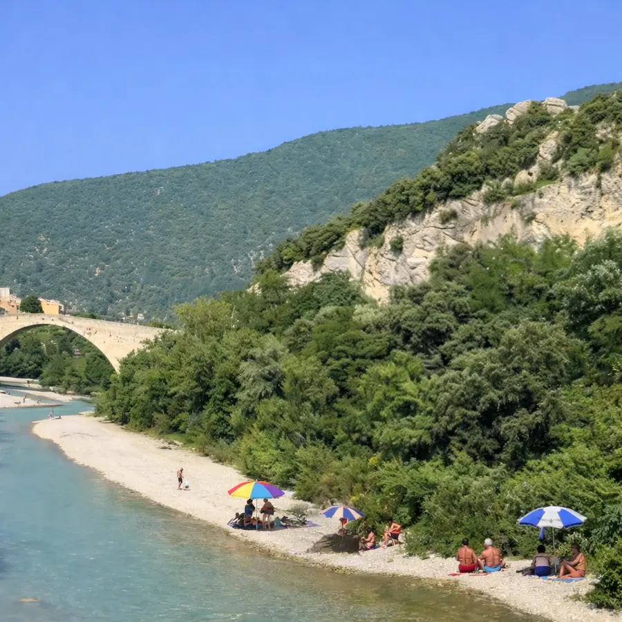 Plage de galets bordée d’arbres et de parasols au bord de l’Eygues, près de Nyons.