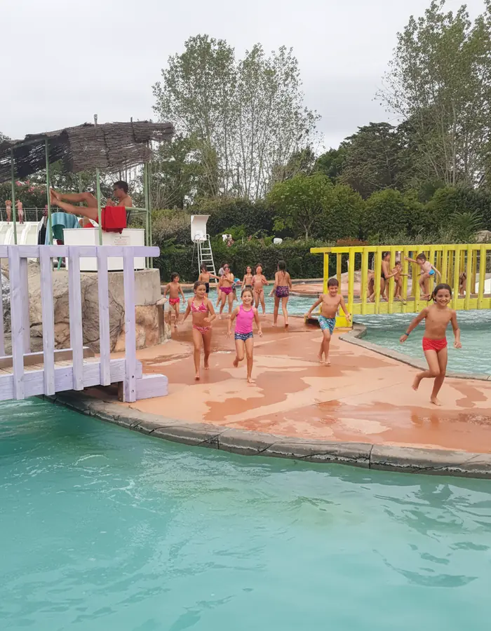 Enfants dans l’espace de jeux d’eau de Nyonsoleïado, près d’un petit pont et d’une barrière jaune.