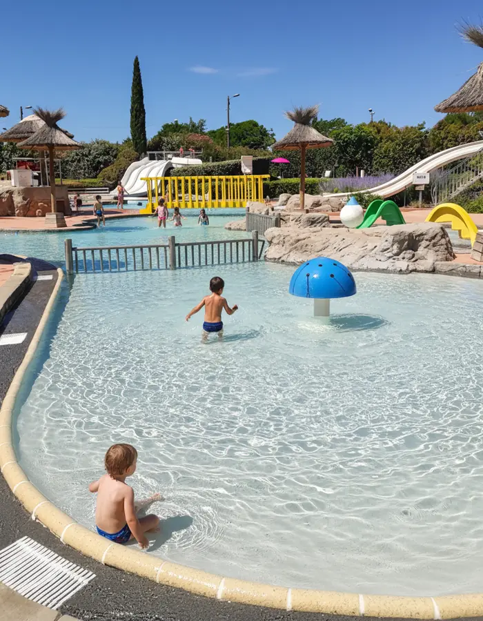 Enfants dans le bassin peu profond de Nyonsoleïado, près des jets d’eau et d’un champignon bleu.