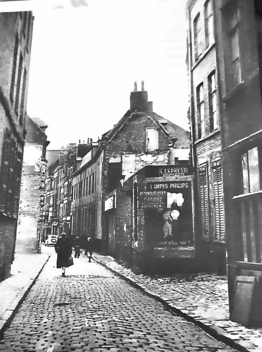Ancienne rue de la Vignette dans le quartier Saint-Sauveur à Lille, avec chaussée pavée, maisons anciennes, publicité Philips et silhouette d'une passante.