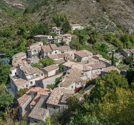 Toits de tuiles et maisons du village de Saint-May, vus en hauteur au milieu des reliefs et des arbres.