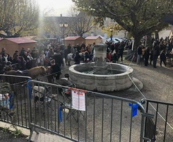 Fontaine sur une place bordée d’arbres, avec des visiteurs et des stands en bois.